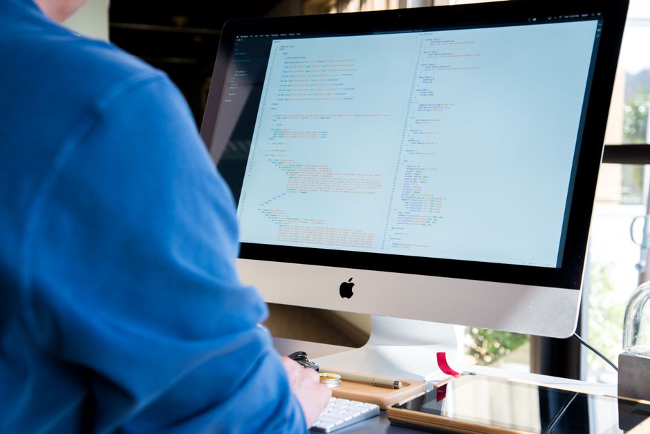 Programer u plavoj košulji kodira na iMac računalu